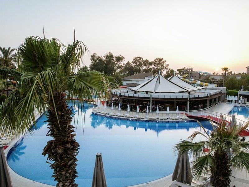 Großer runder Pool mit Bar, umgeben von Palmen und Liegestühlen im Abendlicht.
