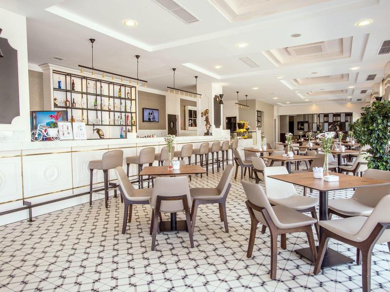 Zona ristorante dell'hotel luminosa e elegante con piastrelle bianche e mobili in legno.