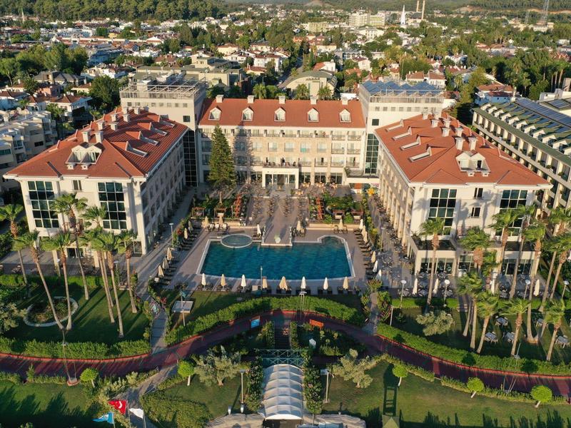 Hotel di lusso con piscina, circondato da palme e ampi edifici.