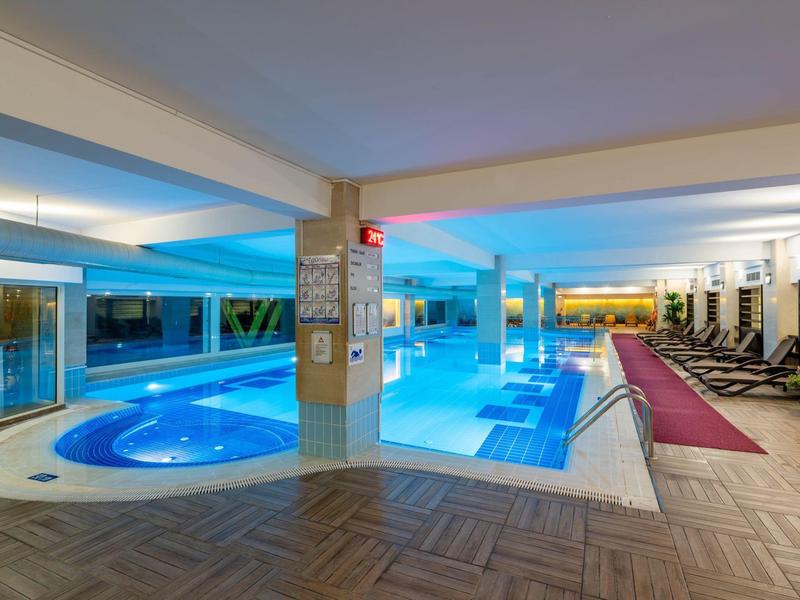 Area interna con piscina riscaldata, vasca idromassaggio e lettini in un hotel moderno.