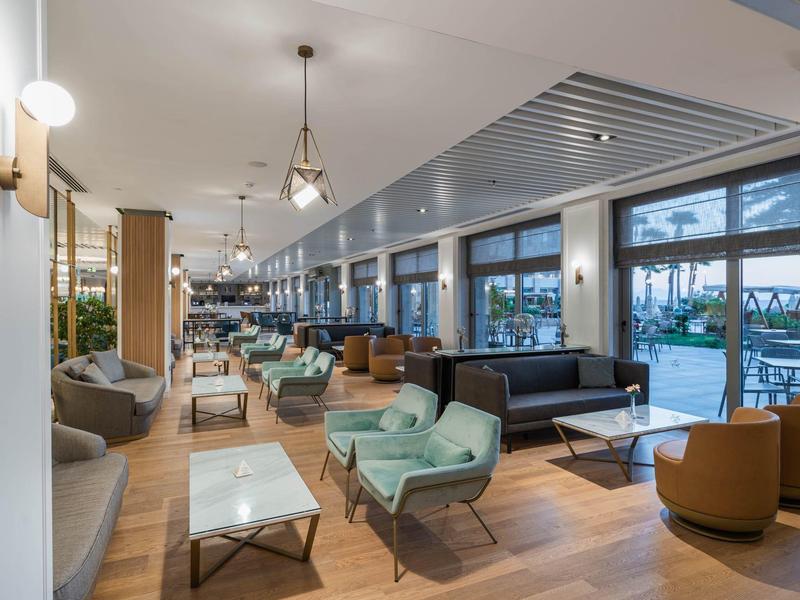 Area lounge dell'hotel moderna con gruppi di sedute e vista su terrazza e piscina.