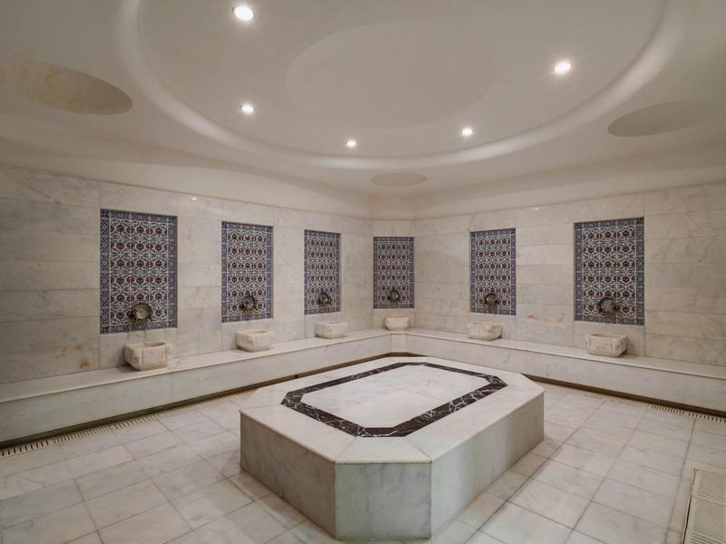 Un lussuoso hammam turco con pareti in marmo, panchine e una vasca centrale per la pulizia.
