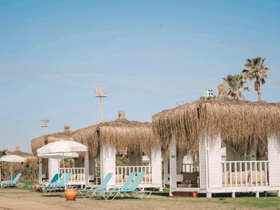 Chalupy s doškovými střechami, lehátka a slunečníky pod jasnou oblohou.