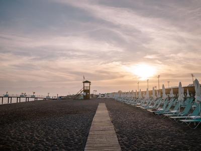 Západ slunce na pláži s dřevěnou cestou, plážovými křesly a věží plavčíka.