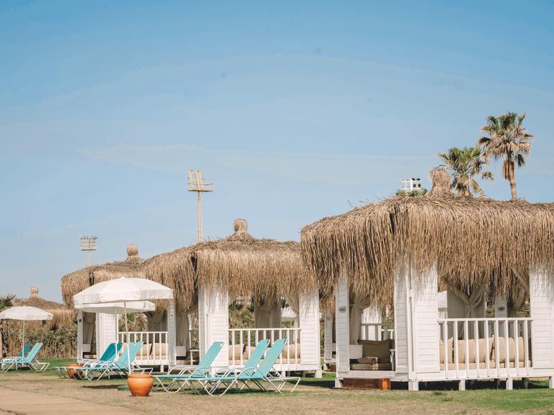 Chalupy s doškovými střechami, lehátka a slunečníky pod jasnou oblohou.