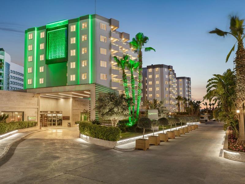 Moderní hotel osvětlený za soumraku s palmami a příjemným dlážděným chodníkem.