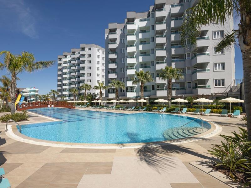 Kruhový venkovní bazén s deštníky a lehátky před moderním hotelem.