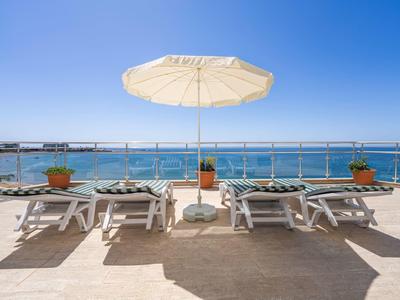 Strandliegen mit Sonnenschirm auf Terrasse mit Meerblick unter klarem Himmel.