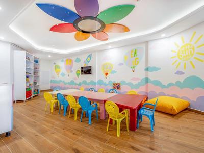 Sala de juegos infantil colorida con mesas pequeñas, sillas y iluminación en forma de flor.