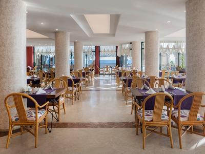 Amplio comedor de hotel con sillas de bambú y mesas con manteles oscuros, piso claro y columnas.