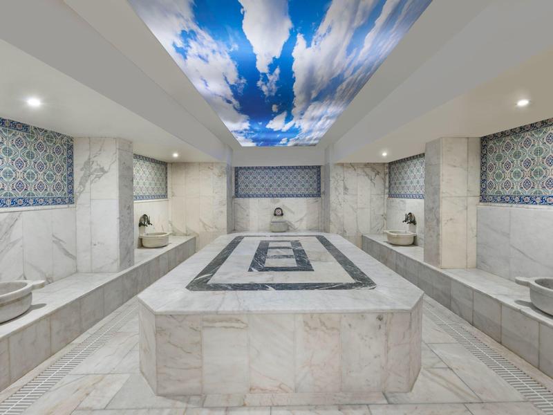 Hammam elegante con lavabos de mármol y azulejos azul y blanco, iluminado por luces en el techo con motivo de cielo.