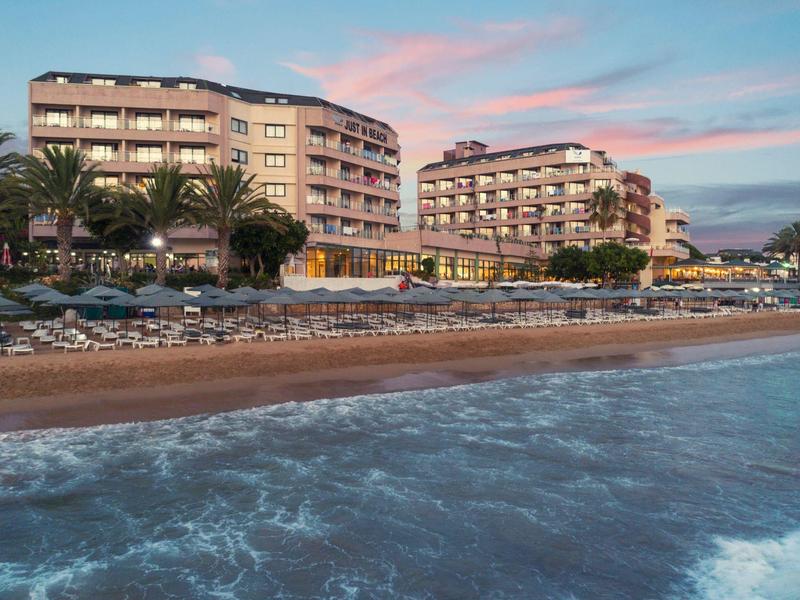 Edificios de hotel en la playa con tumbonas y palmeras al atardecer.