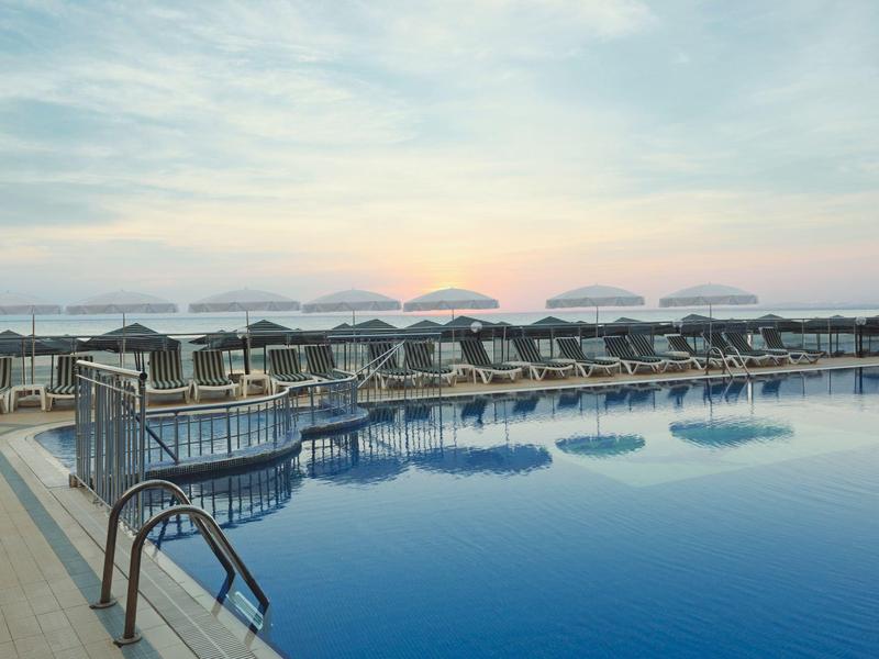 Gran piscina con tumbonas y sombrillas al atardecer en un lugar de vacaciones.