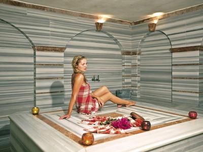 Femme assise dans un hammam turc traditionnel avec des murs et un sol en marbre.