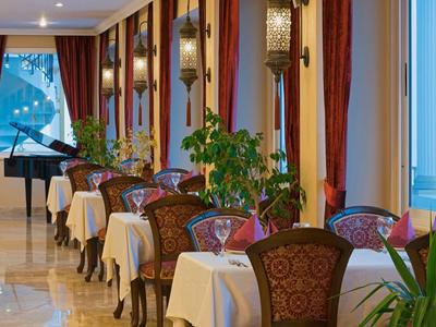 Salle à manger élégante avec nappes blanches, plantes décoratives et un piano à queue noir en arrière-plan.