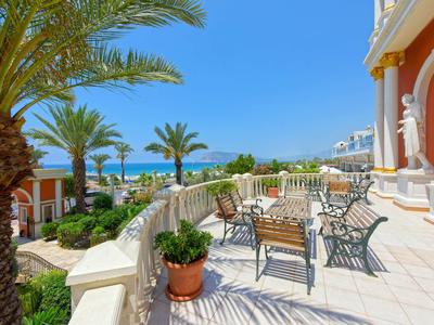 Słoneczny taras hotelowy z widokiem na ogród, krzesłami i palmami pod niebieskim niebem.