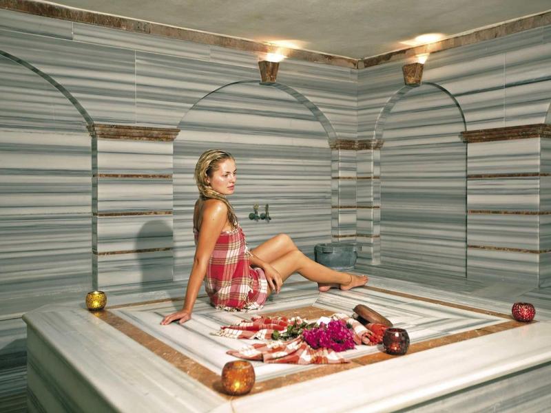 Femme assise dans un hammam turc traditionnel avec des murs et un sol en marbre.