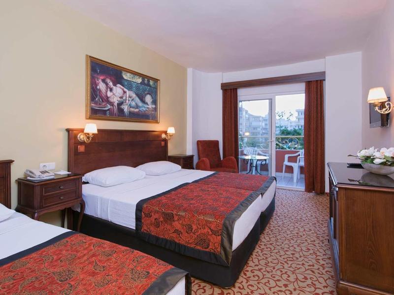 Chambre d'hôtel avec deux lits, bureau, chaise et balcon donnant sur le jardin.