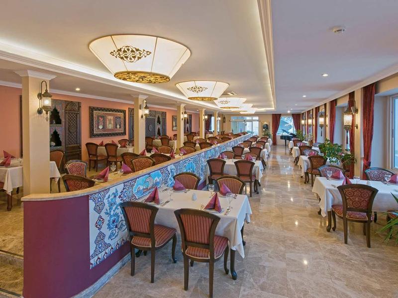 Salle à manger élégante avec tables dressées, chaises et grand lustre dans un hôtel.
