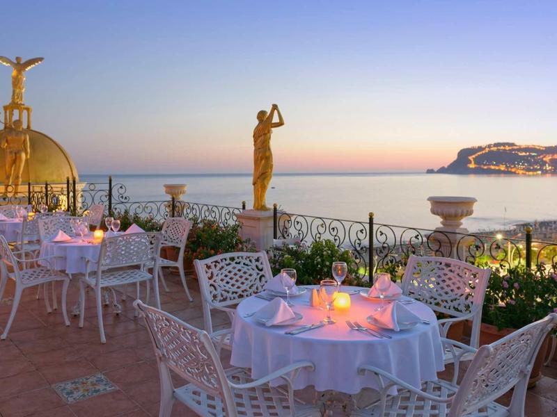 Terrasse avec tables dressées donnant sur la mer au coucher du soleil.