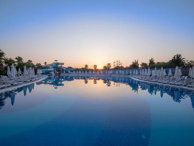 Grande piscine avec chaises longues et parasols au coucher du soleil dans une station.