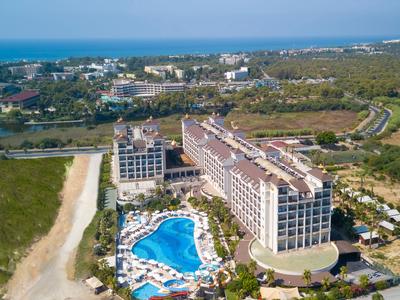 Grand bâtiment hôtelier avec une grande piscine bleue et paysage environnant au bord de la mer.
