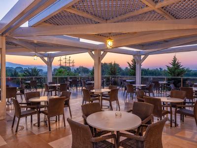 Espace de restaurant ouvert avec tables et chaises sous une structure en bois couverte au coucher du soleil.
