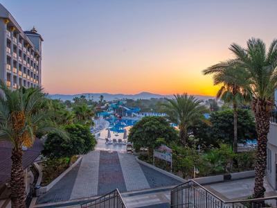 Vue d'un complexe avec piscine, palmiers et montagnes au coucher du soleil.
