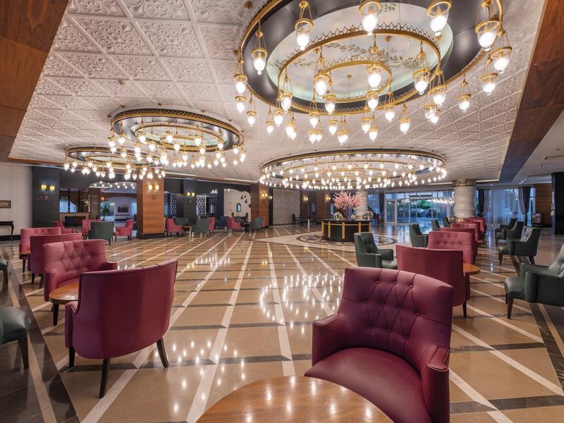 Lobby d'hôtel élégante avec grands lustres, fauteuils rouges et sol en marbre brillant.
