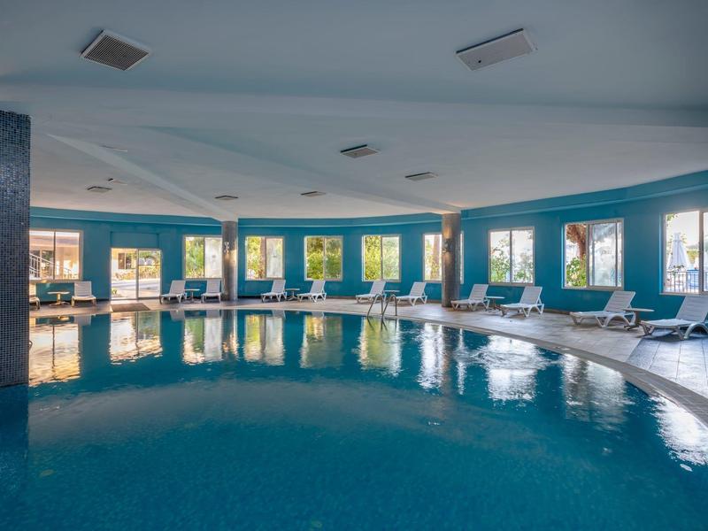 Piscine intérieure suédoise avec murs bleus, chaises longues et grandes fenêtres.