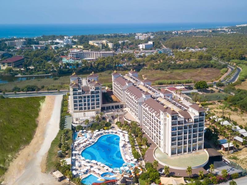Vue aérienne d'un grand hôtel avec piscine près de la côte entouré de verdure.