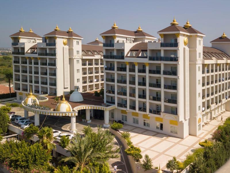 Grand hôtel à plusieurs étages avec palmiers et jardin bien entretenu sous un ciel dégagé