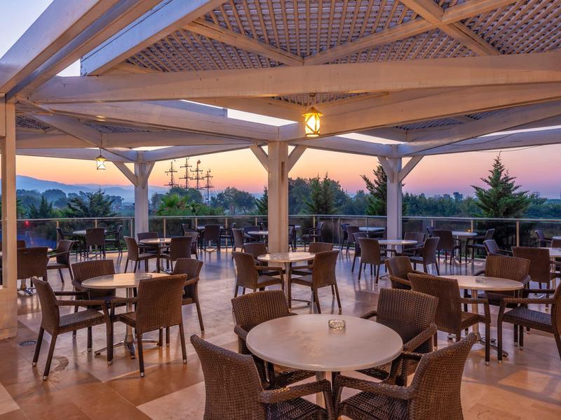Espace de restaurant ouvert avec tables et chaises sous une structure en bois couverte au coucher du soleil.