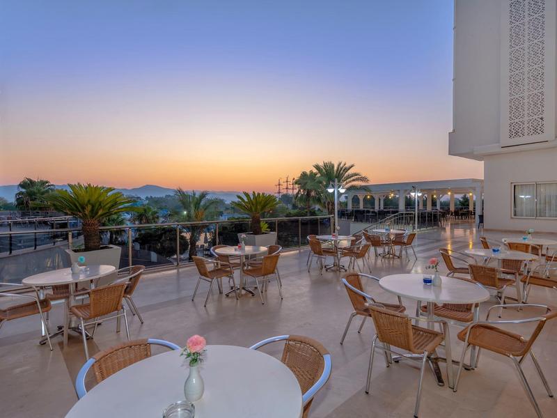 Espace extérieur d'hôtel avec tables et chaises, vue sur la mer au coucher du soleil.