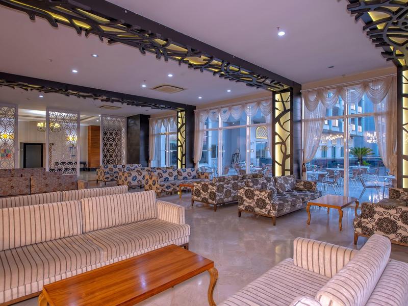 Espace lounge élégant d'hôtel avec mobilier rembourré et grandes fenêtres donnant sur la terrasse extérieure.