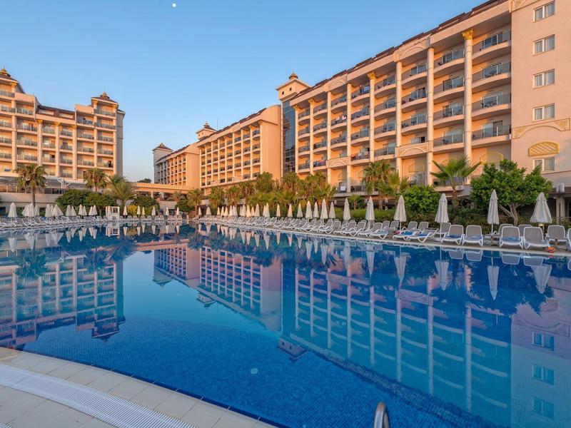 Grande piscine devant des bâtiments d'hôtel modernes au coucher du soleil avec réflexion claire.
