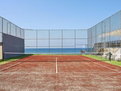 Campo da tennis con superficie rossa e vista mare sotto cielo limpido.