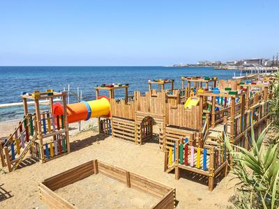 Dětské hřiště s dřevěnými konstrukcemi a barevným tunelem na písečné pláži u moře