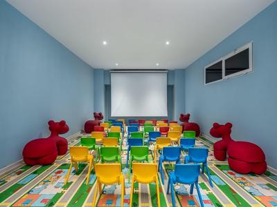 Barevná kino místnost s malými židlemi a červenými dětskými sedadly, modré stěny a pestrý koberec.