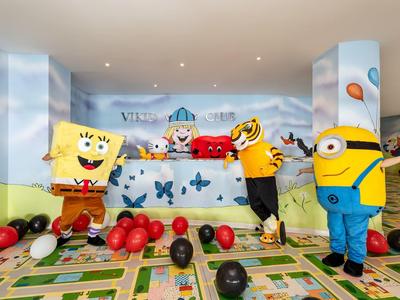 Děti si hrají s nafukovacími postavičkami v barevném vnitřním prostoru s balónky.