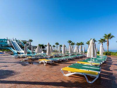 Prázdná lehátka a slunečníky u hotelového bazénu pod jasně modrou oblohou.