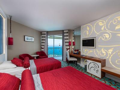 Camera d'hotel con tre letti rossi, vista mare e decorazione murale.