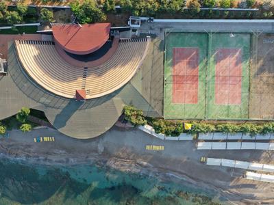 Vista aerea di un anfiteatro accanto a campi da tennis sulla costa.