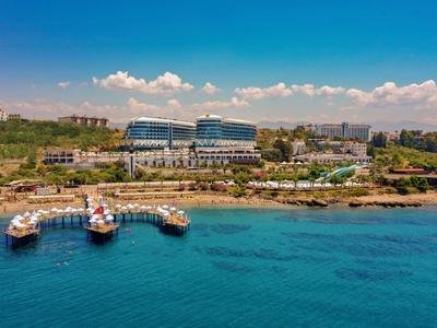 Luxusní hotel na břehu s přístavem a čistou modrou vodou pod slunečnou oblohou.