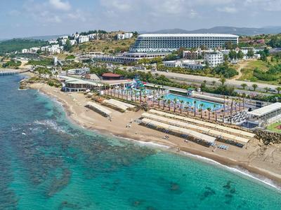 Pobřežní oblast s čistou vodou, lehátky, slunečníky a hotely v pozadí.