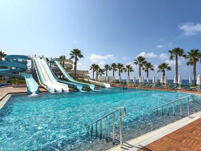Velký bazén s vodními skluzavkami a palmami na slunné dovolené.