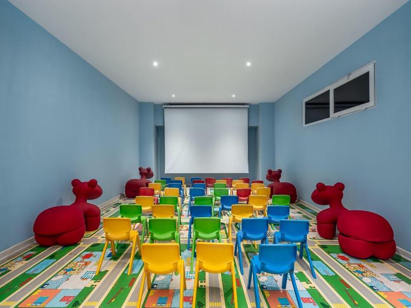 Barevná kino místnost s malými židlemi a červenými dětskými sedadly, modré stěny a pestrý koberec.