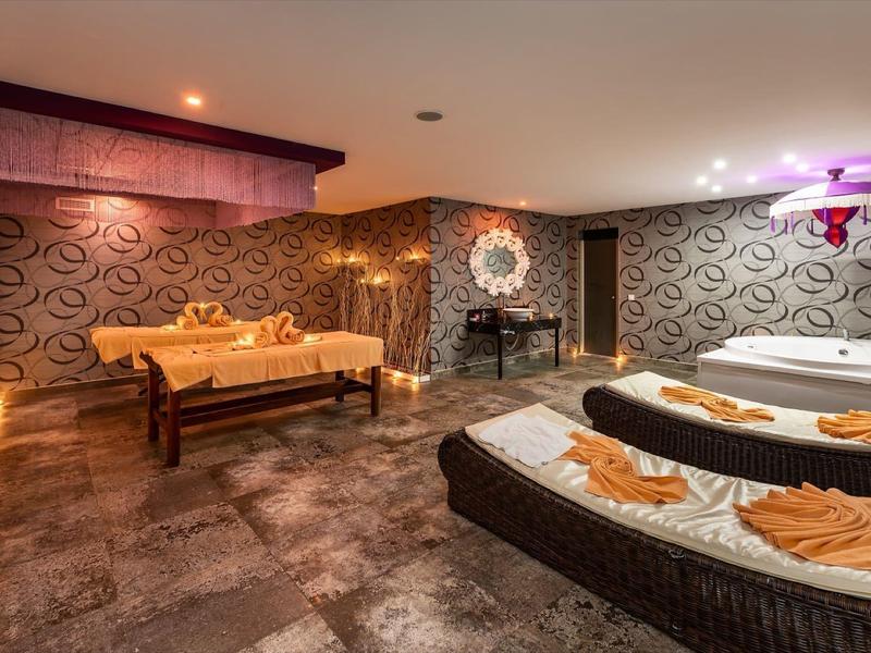 Pohodlná wellness místnost se dvěma masážními stoly, pohovkou a ambientním osvětlením.