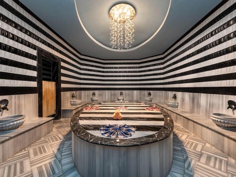 Luxusní hammam s mramorovými stěnami, centrálním umyvadlem a starožitným osvětlením.