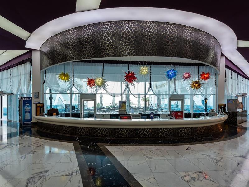 Moderní hotelová lounge s kulatým barem a barevnými květinovými lampami na stropě.